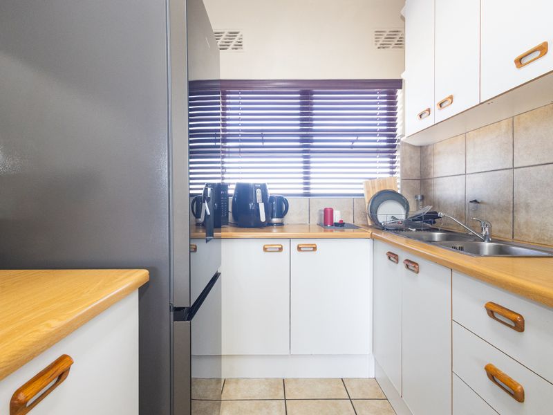 A functional kitchen featuring white cabinetry, laminate countertops, a stainless steel double sink, and tiled backsplash with neutral floor tiles.
