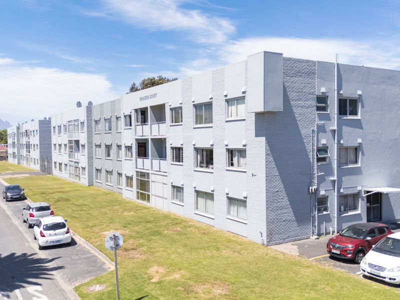 Exterior view of Bracken Court apartment complex featuring a painted brick facade, multiple balconies, and dedicated parking area.