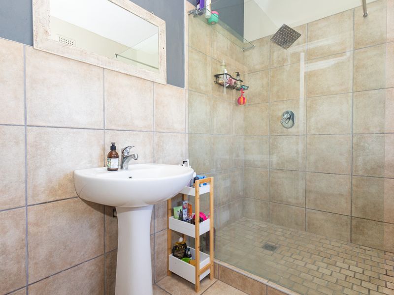 A functional bathroom featuring a pedestal basin, mixer tap, and a spacious walk-in shower with a rainfall shower head and glass enclosure.