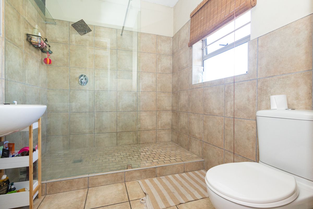 A functional bathroom featuring a walk-in shower with a glass screen, tiled walls and flooring, a basin, and a toilet.