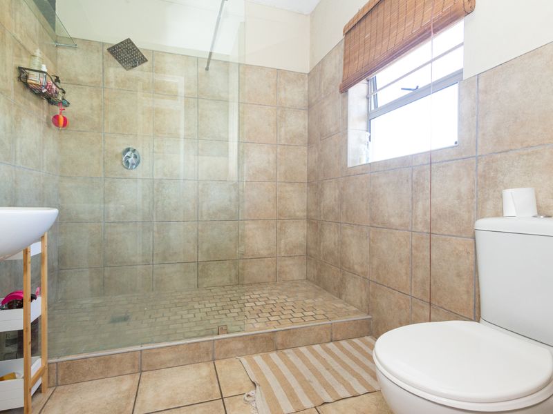 A functional bathroom featuring a walk-in shower with a glass screen, tiled walls and flooring, a basin, and a toilet.