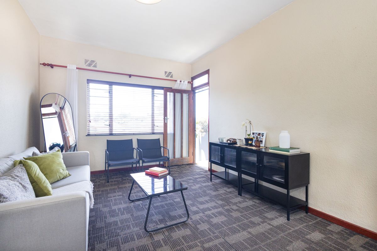 A living room featuring carpet flooring, a large window, and a glass-panelled door providing access to an outdoor area.