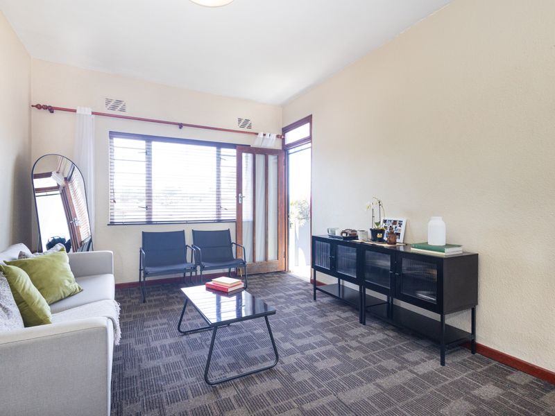 A living room featuring carpet flooring, a large window, and a glass-panelled door providing access to an outdoor area.
