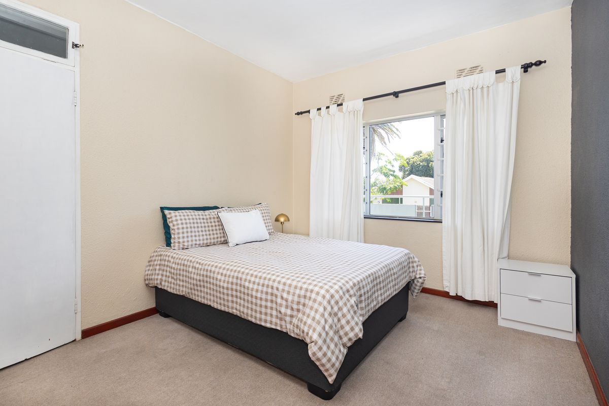 A well-lit bedroom featuring neutral walls, carpeted flooring, and a built-in cupboard, offering a comfortable and functional living space.