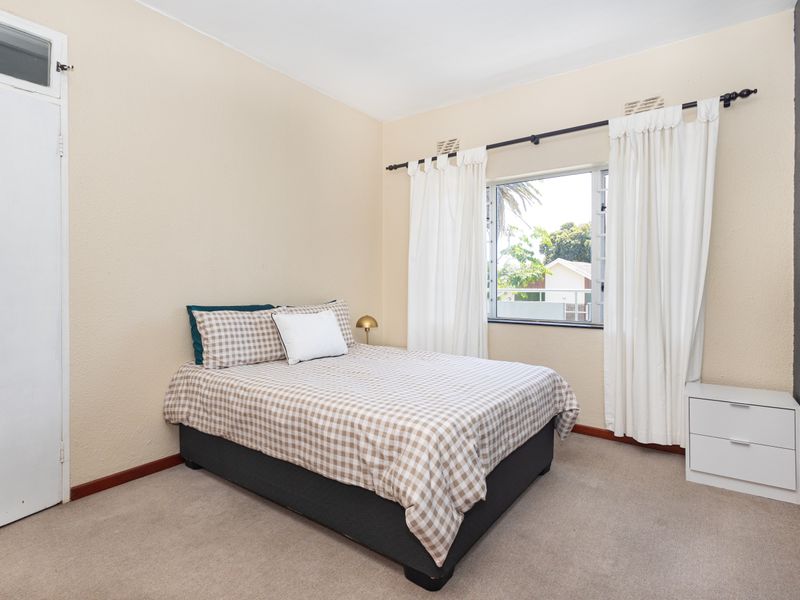 A well-lit bedroom featuring neutral walls, carpeted flooring, and a built-in cupboard, offering a comfortable and functional living space.