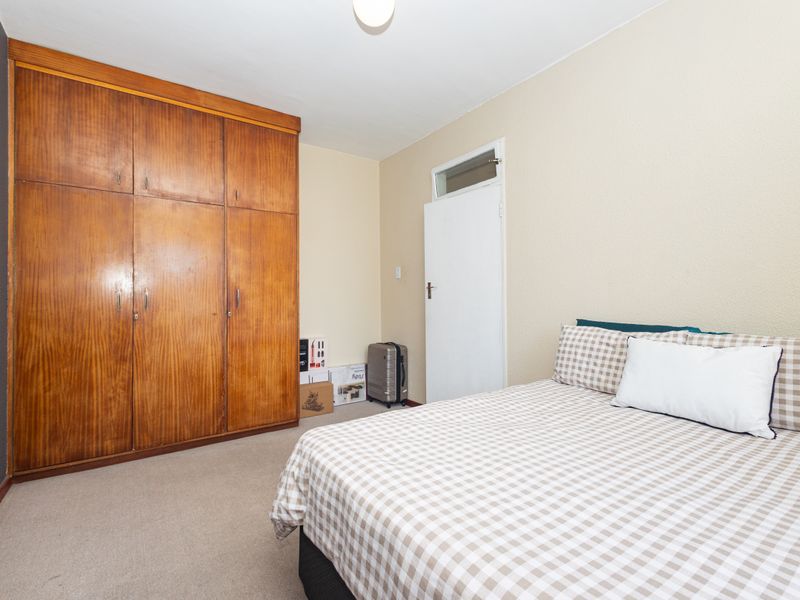 A bedroom featuring a large built-in wooden wardrobe, carpeted flooring, and a transom window above the door.