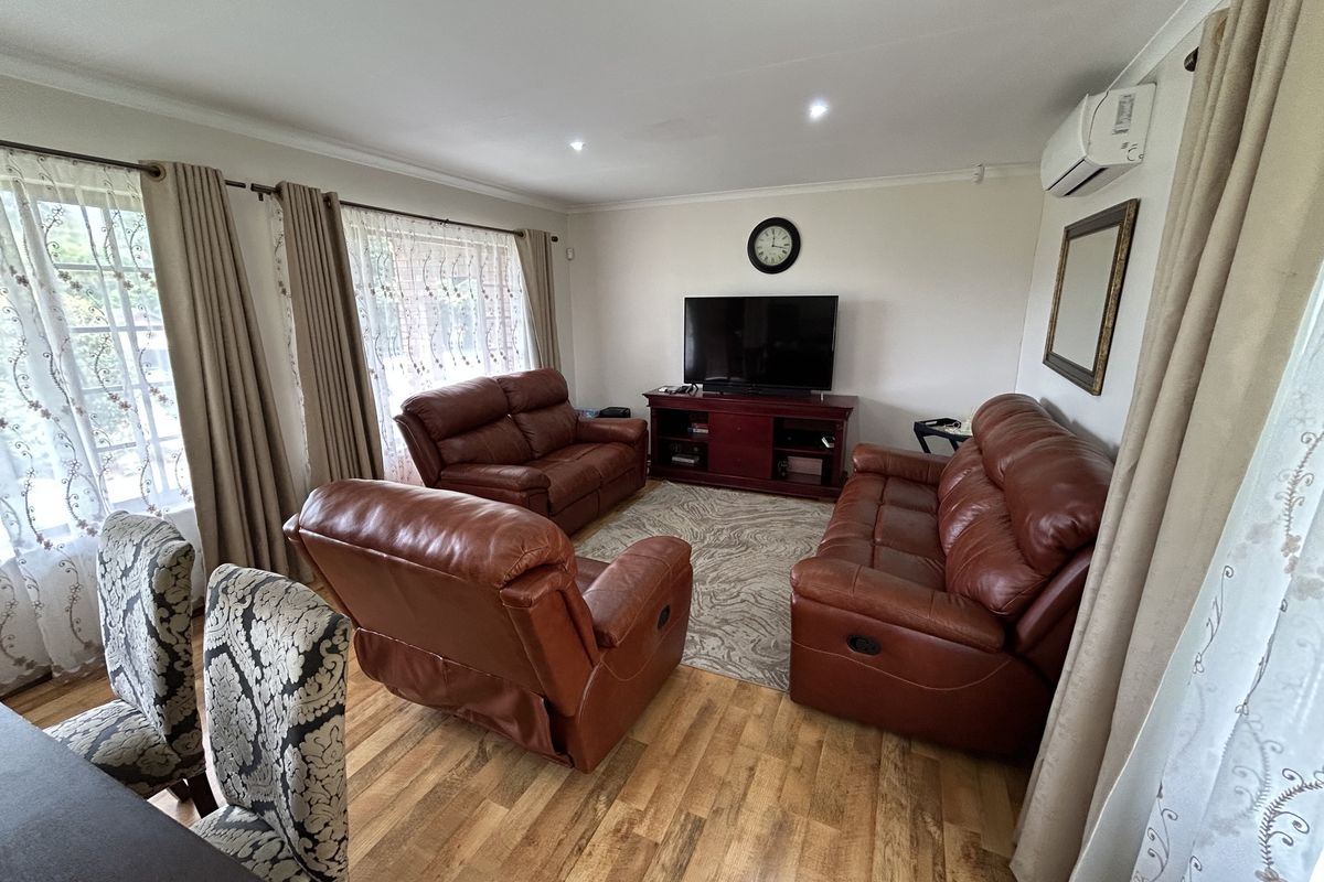 A comfortable living room featuring laminate flooring, recessed downlighting, and a wall-mounted split-system air conditioning unit.