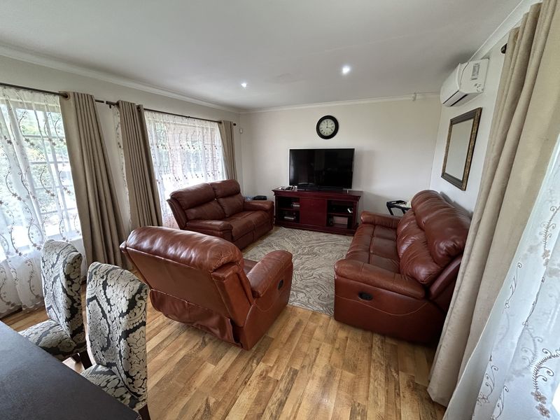 A comfortable living room featuring laminate flooring, recessed downlighting, and a wall-mounted split-system air conditioning unit.
