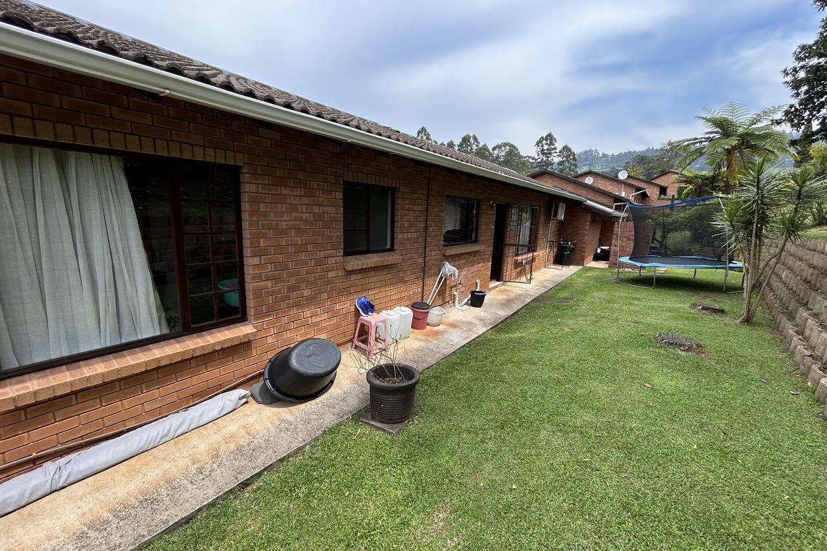 Rear view of the townhouse featuring a brick facade, tiled roof, and a concrete walkway leading along the lawn and retaining wall.