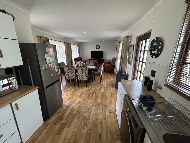 Spacious open-plan living and dining area featuring laminate flooring, integrated kitchen cabinetry, and direct access to the exterior through a timber-framed glass door.