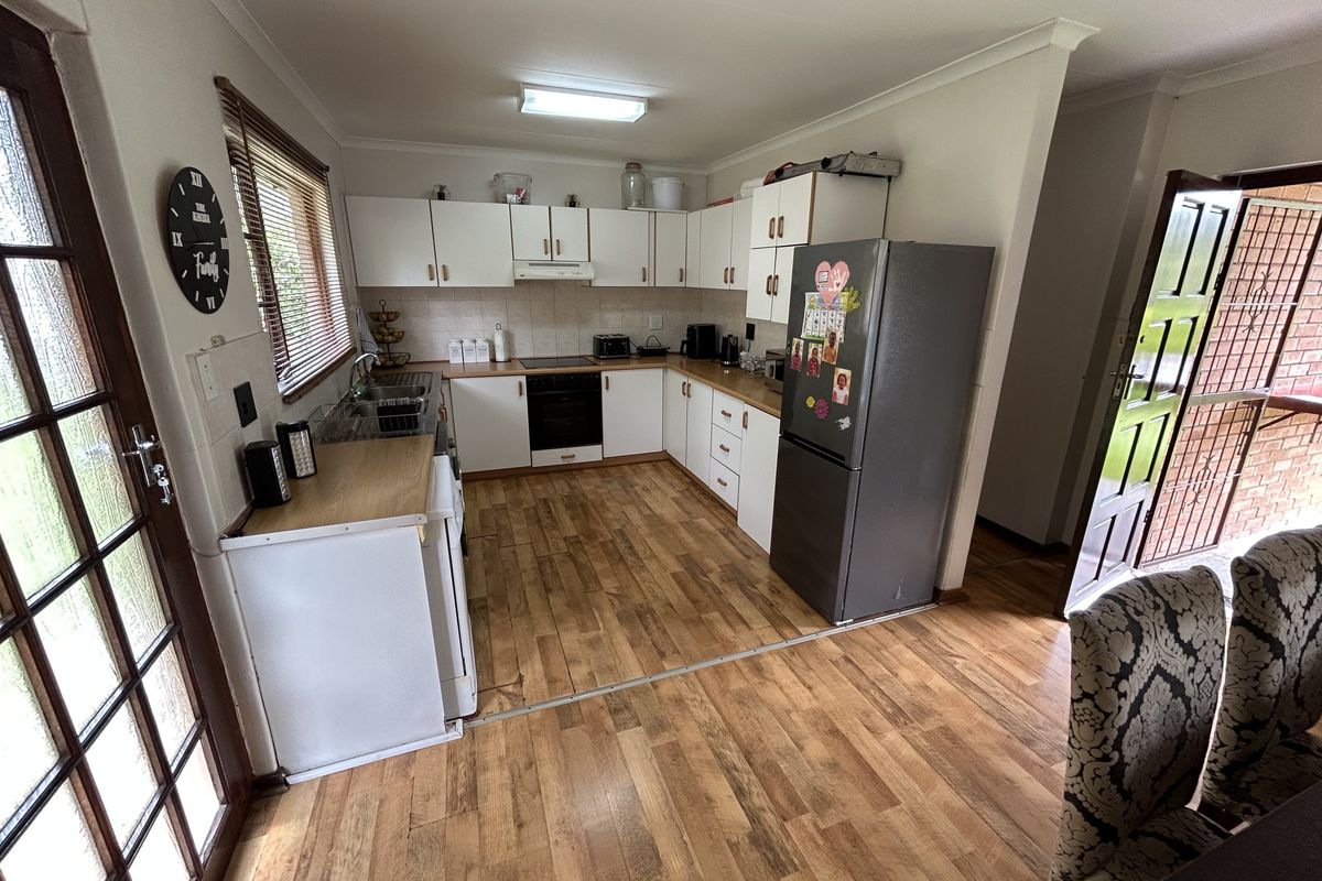 A functional kitchen featuring white cabinetry, laminate countertops, integrated oven and hob, and wood-look laminate flooring with direct access to the exterior.