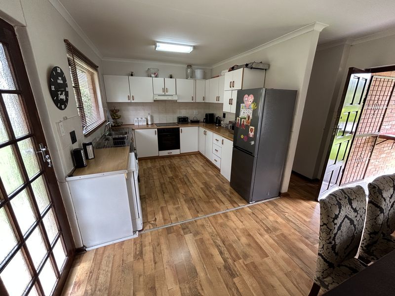 A functional kitchen featuring white cabinetry, laminate countertops, integrated oven and hob, and wood-look laminate flooring with direct access to the exterior.