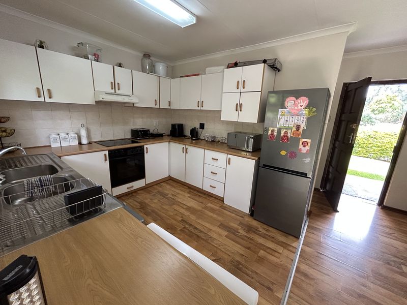 A functional kitchen featuring white cabinetry, laminate countertops, integrated oven and hob, and wood-look flooring with direct access to the exterior.