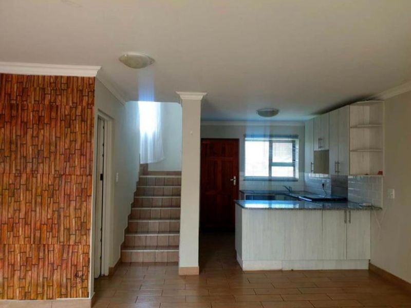Open plan living area featuring a kitchen with built-in cabinetry, granite countertops, and a staircase leading to the upper level.