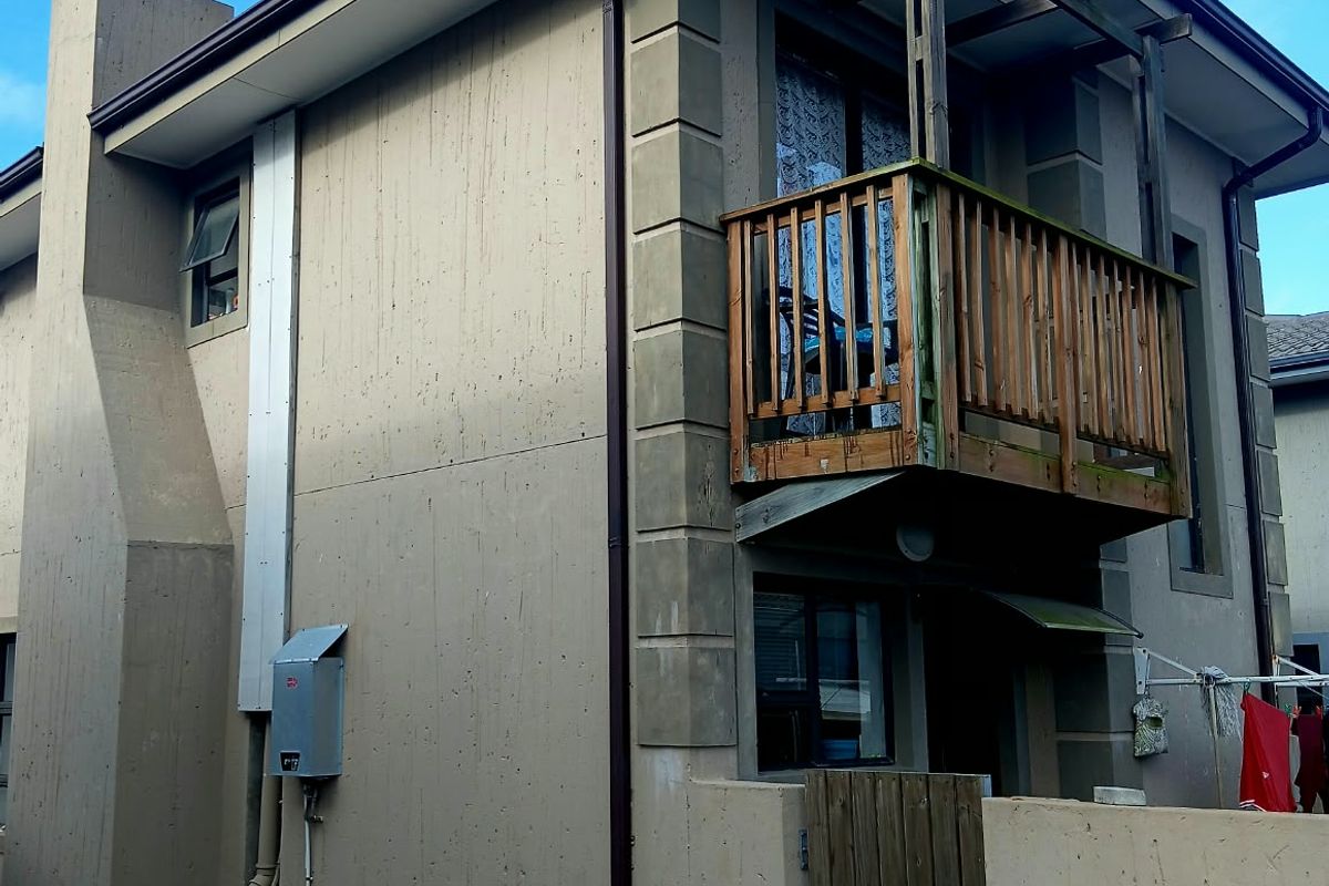Rear elevation of the property featuring a timber balcony, chimney stack, and paved access area with external utility connections.