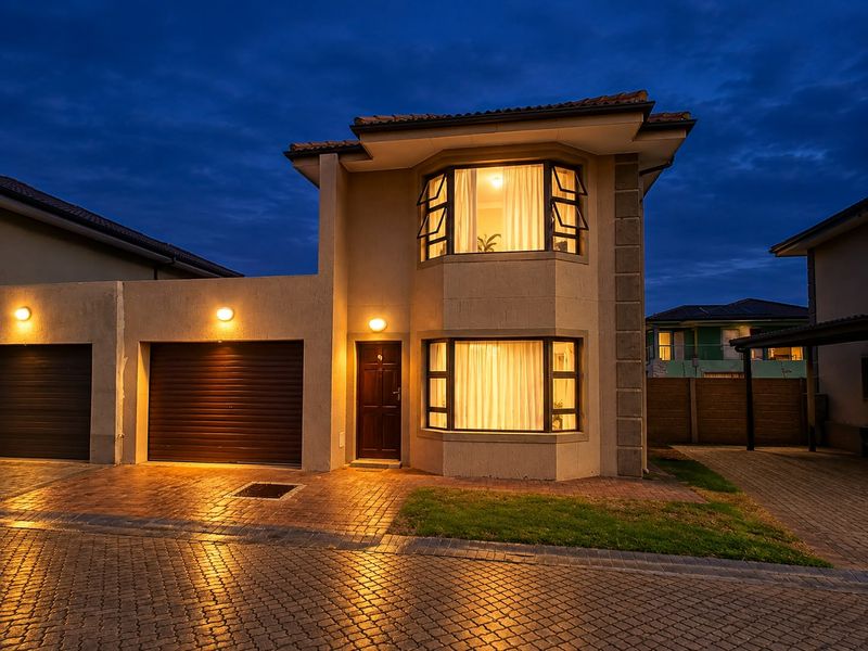 A well-maintained double-story residential property featuring a paved driveway, double garage, and distinctive bay windows, captured during twilight.