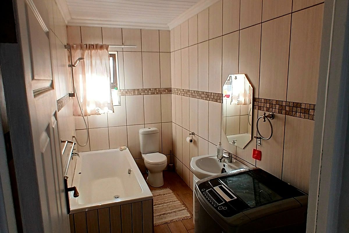 A functional bathroom featuring a bathtub, pedestal basin, and toilet, finished with neutral wall tiles and wood-look floor tiles.