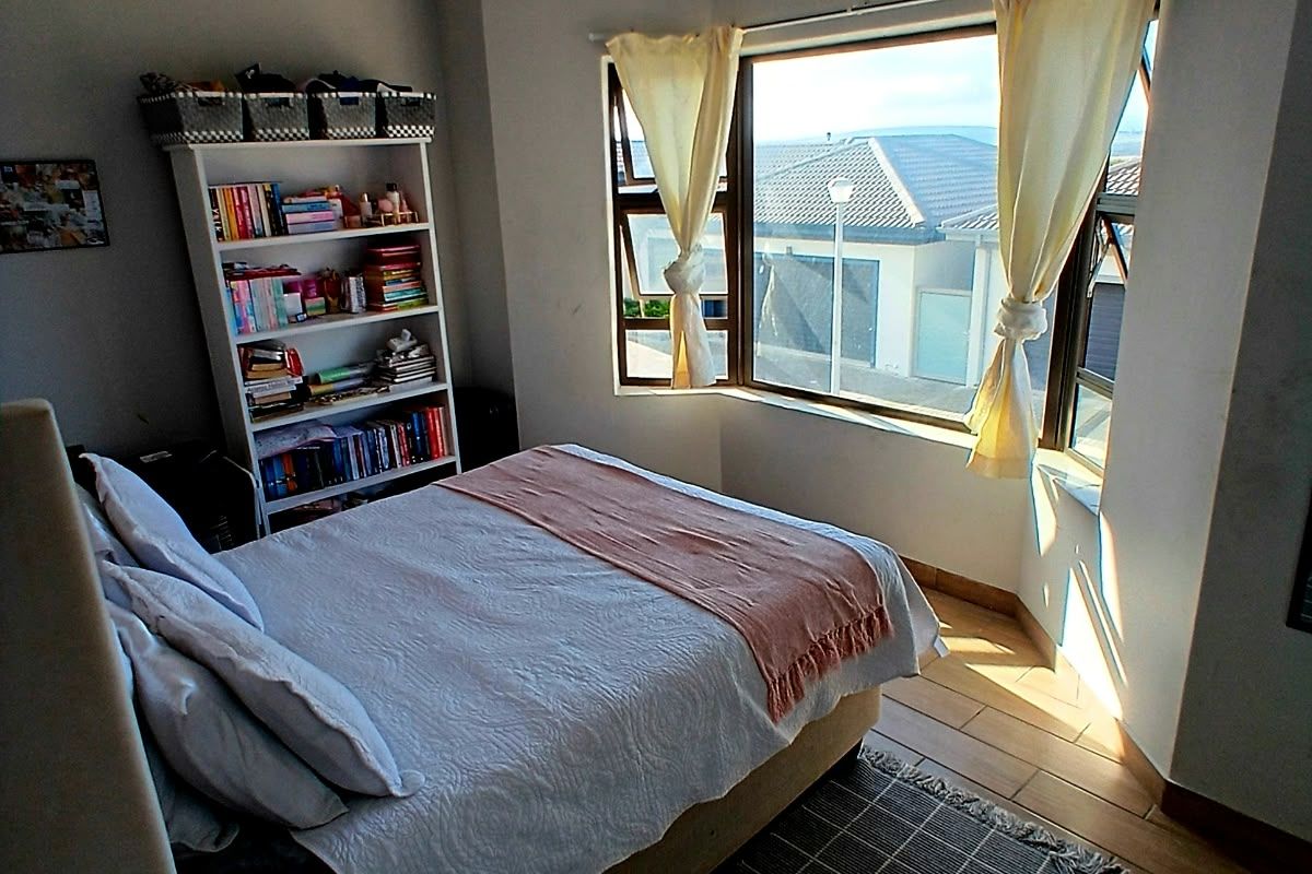 A bright bedroom featuring a large bay window, timber-look tiled flooring, and a classic tongue and groove ceiling with cove cornicing.