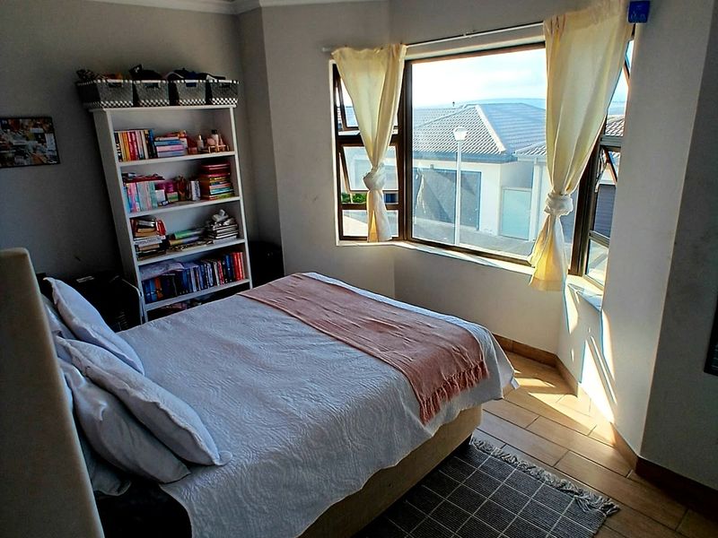 A bright bedroom featuring a large bay window, timber-look tiled flooring, and a classic tongue and groove ceiling with cove cornicing.