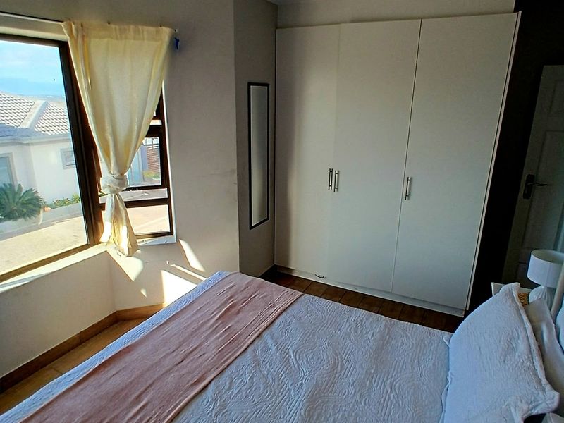 A well-lit bedroom featuring built-in cupboards, a bay window, and a classic tongue and groove ceiling with wooden flooring.