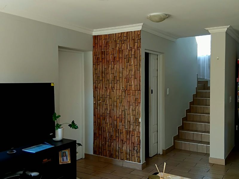A living room featuring tiled flooring, a staircase, and a decorative feature wall, providing a functional and connected layout.