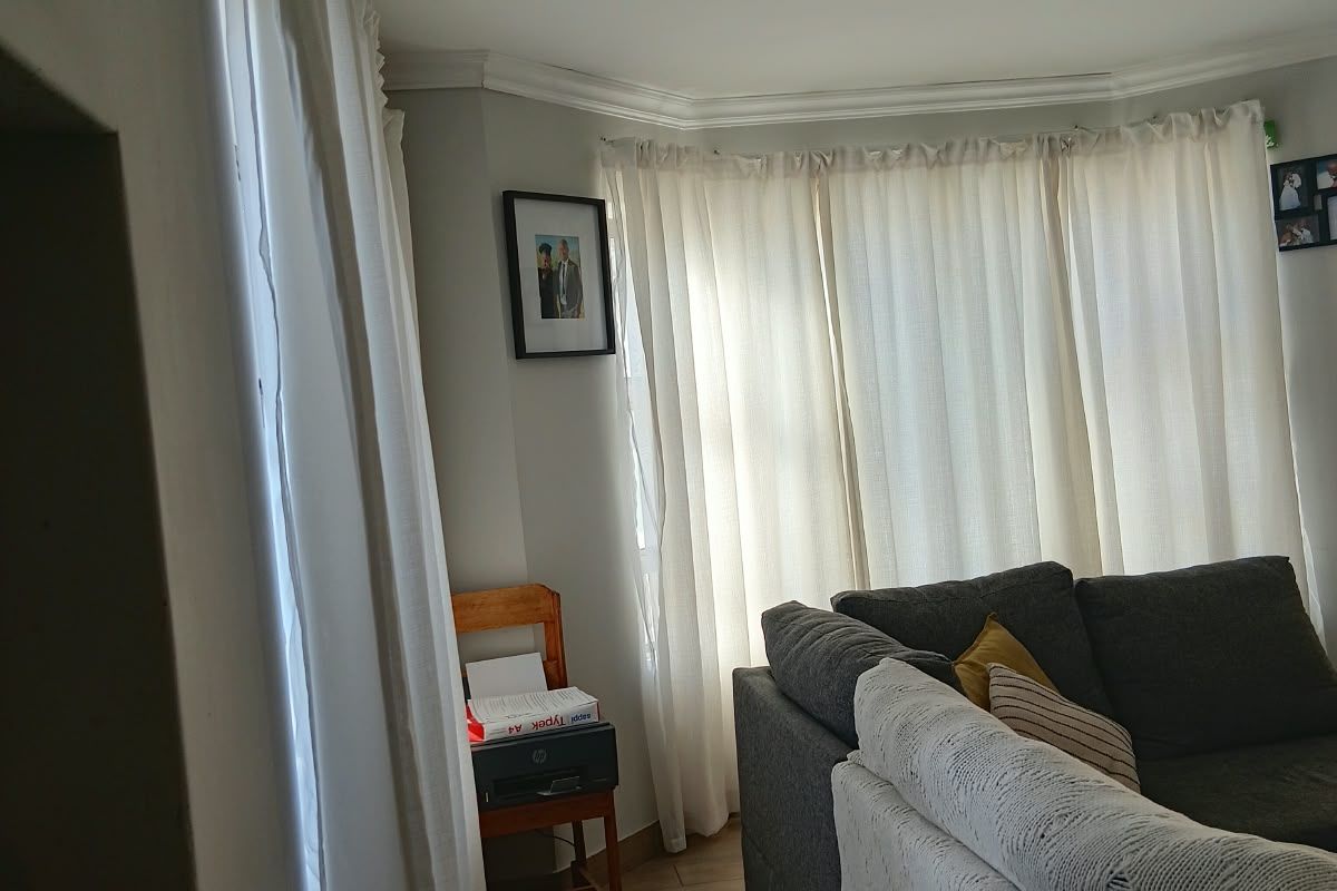 A living room area featuring a bay window with curtains, tiled flooring, and decorative ceiling cornicing.
