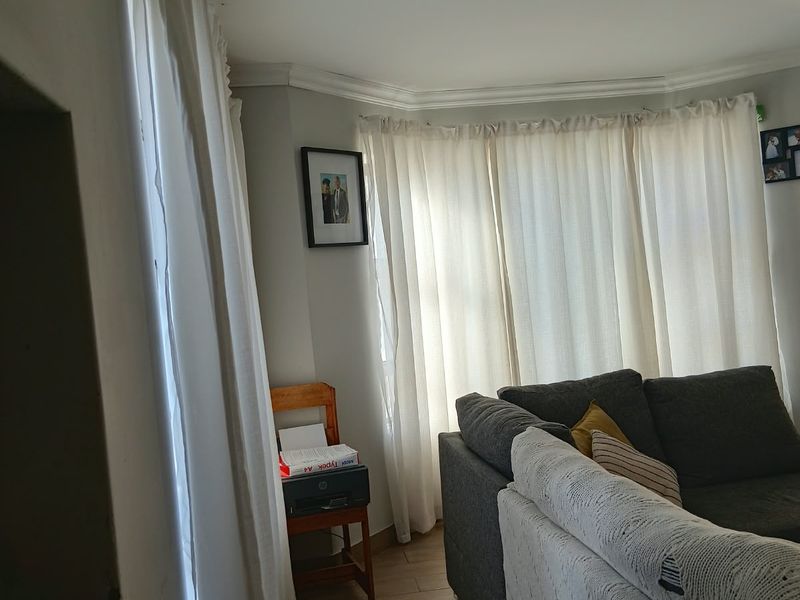 A living room area featuring a bay window with curtains, tiled flooring, and decorative ceiling cornicing.