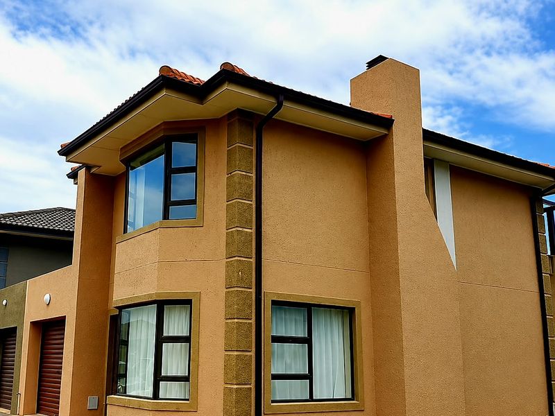 A well-maintained two-story residential property featuring a stucco facade, bay windows, a prominent chimney, and a paved driveway.