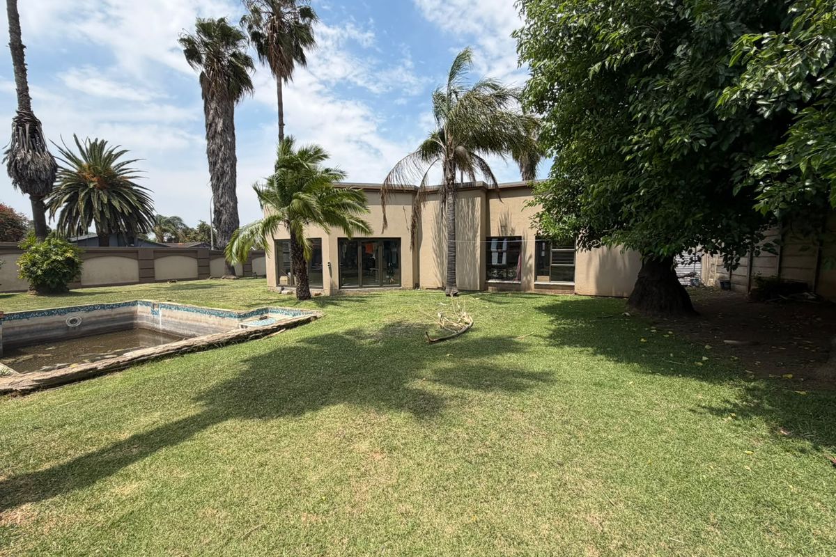 Rear view of the property featuring a spacious garden, established trees, and a swimming pool with surrounding boundary wall.