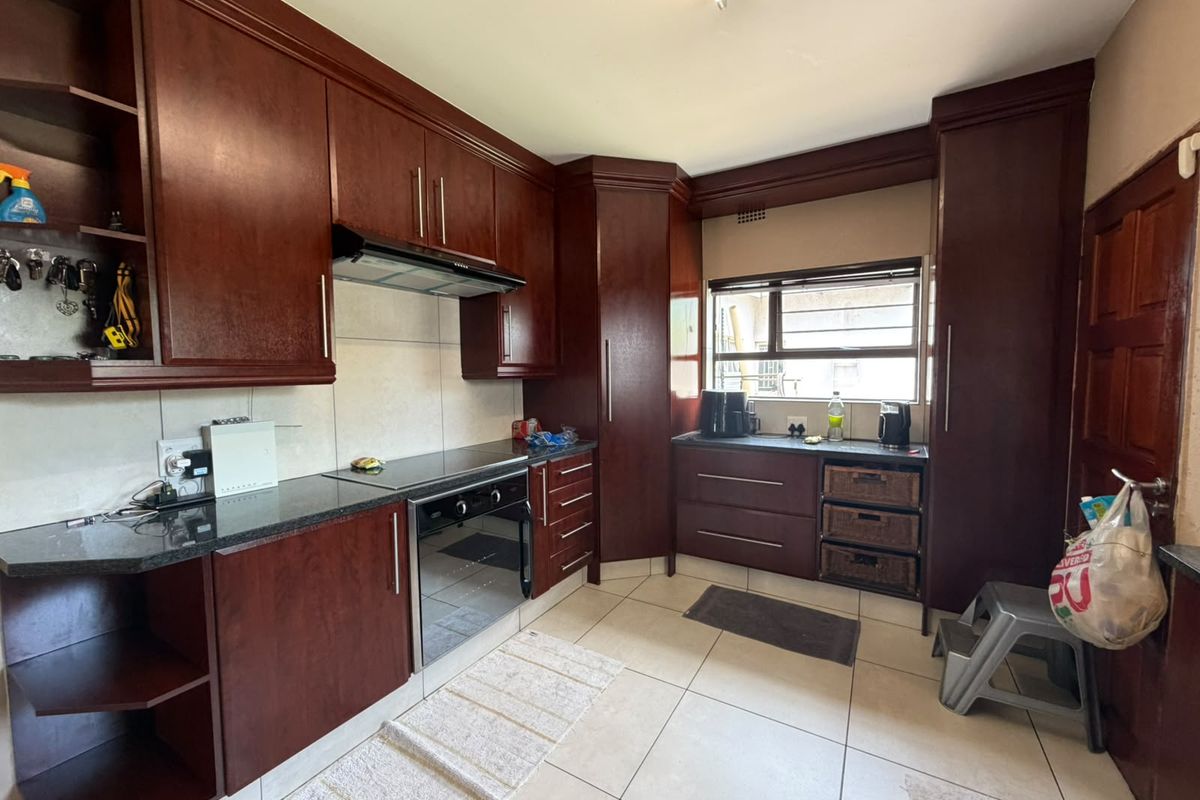 A functional kitchen featuring dark wood cabinetry, granite countertops, built-in oven and hob, and tiled flooring throughout.