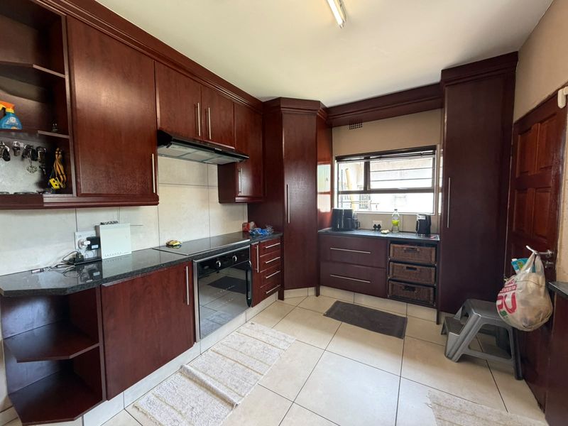 A functional kitchen featuring dark wood cabinetry, granite countertops, built-in oven and hob, and tiled flooring throughout.