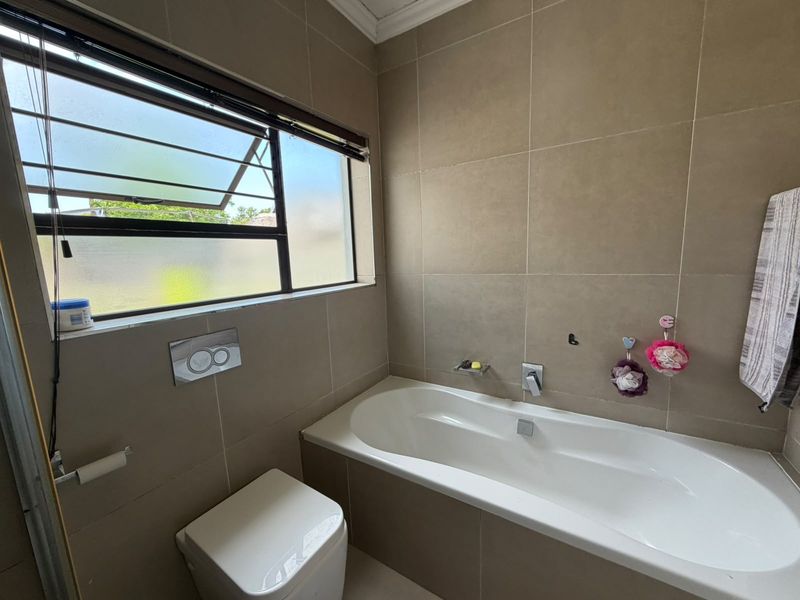 A modern bathroom featuring a built-in bathtub, wall-mounted toilet with a concealed cistern, and neutral wall tiling.