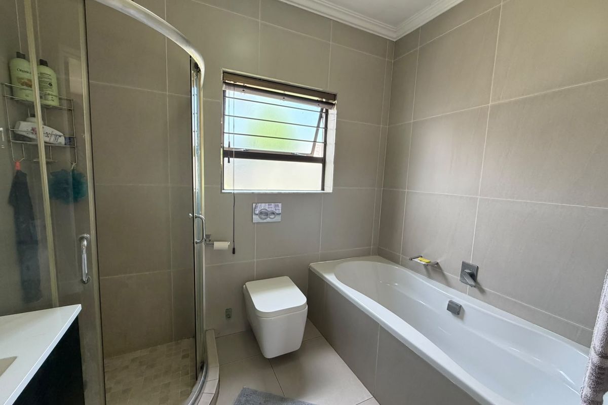 Modern bathroom featuring a glass shower enclosure, built-in bathtub, wall-hung toilet with concealed cistern, and neutral floor-to-ceiling wall tiles.
