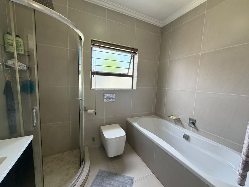 Modern bathroom featuring a glass shower enclosure, built-in bathtub, wall-hung toilet with concealed cistern, and neutral floor-to-ceiling wall tiles.