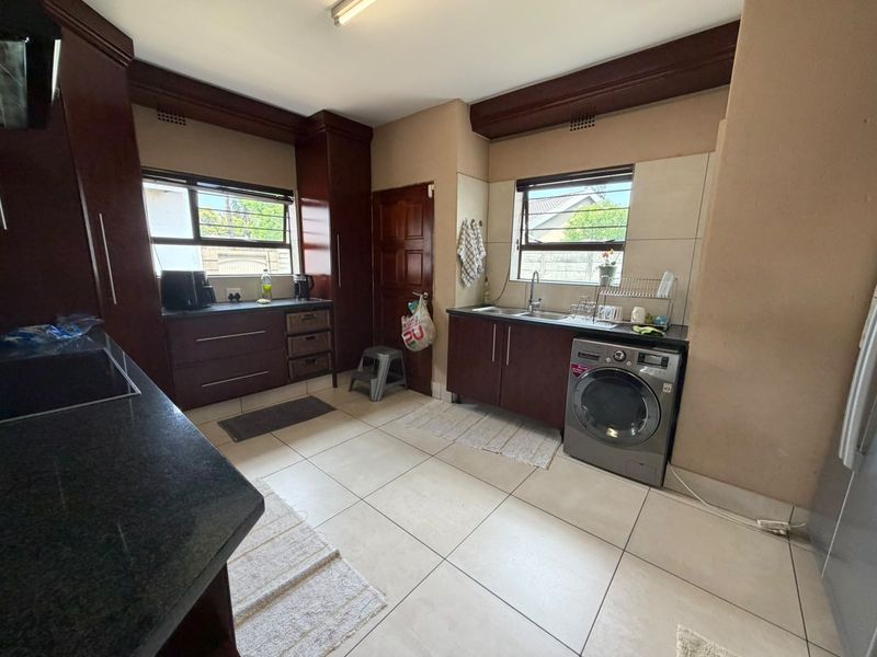 A functional kitchen featuring dark wood cabinetry, granite countertops, tiled flooring, and integrated laundry plumbing, offering a practical layout for daily use.