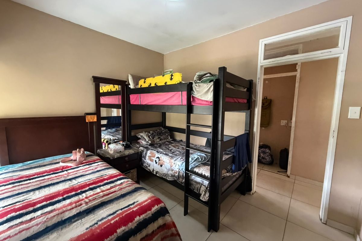 A functional bedroom featuring tiled flooring and a doorway leading to an adjacent space, with neutral wall tones and standard lighting.