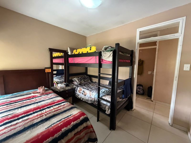 A functional bedroom featuring tiled flooring and a doorway leading to an adjacent space, with neutral wall tones and standard lighting.
