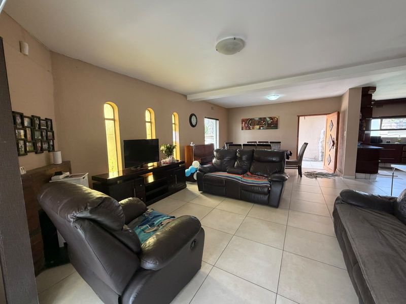 Spacious open-plan living and dining area featuring neutral tiled flooring, arched windows, and direct access to the kitchen and outdoor space.
