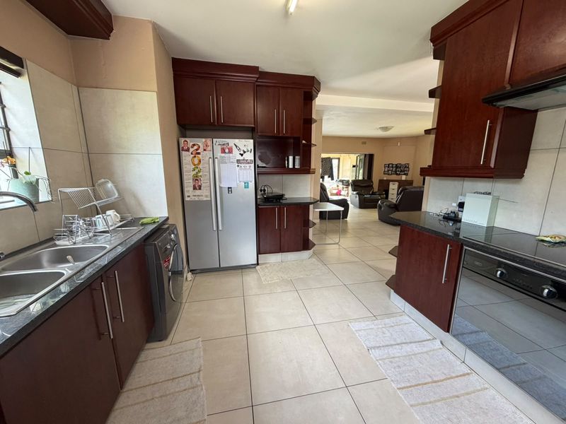 Open plan kitchen featuring dark wood cabinetry, granite countertops, and integrated appliances, flowing into the adjacent living area with tiled flooring throughout.