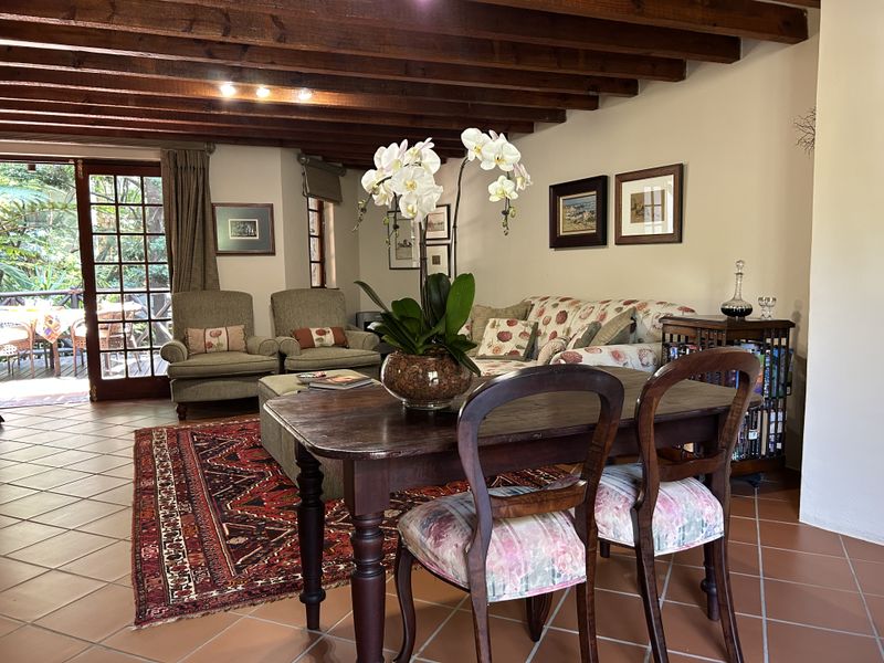 A cozy living area featuring exposed timber ceiling beams, terracotta floor tiles, and large french doors providing direct access to an outdoor patio space.