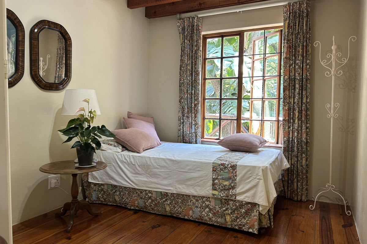 A cozy bedroom featuring warm timber flooring and exposed ceiling beams, complemented by a large casement window that allows for natural light.