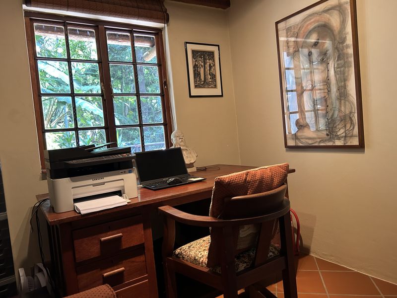 A cozy home office featuring terracotta floor tiles, a wooden window frame with a bamboo blind, and a warm, inviting atmosphere.