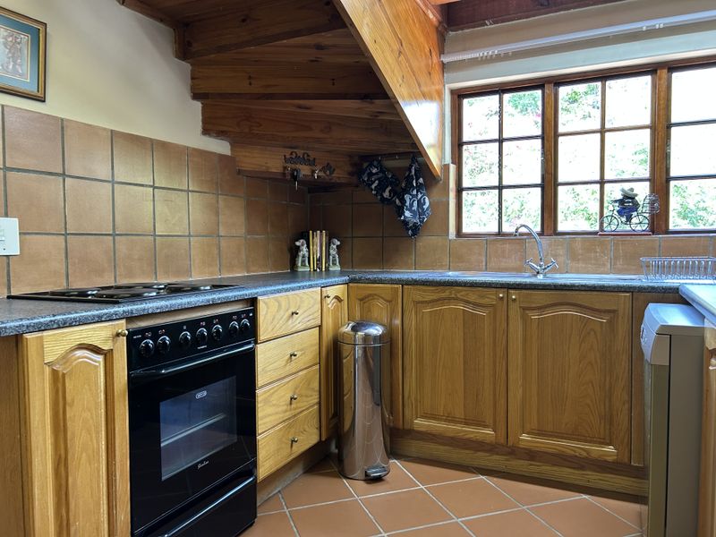 A functional kitchen featuring wooden cabinetry, tiled backsplash, built-in oven with hob, and a stainless steel sink under a window.