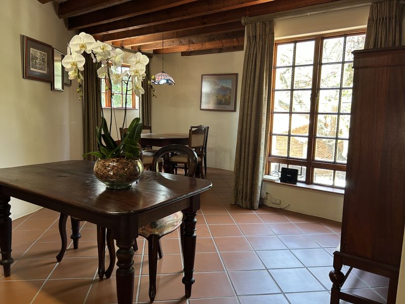 A charming dining room featuring exposed timber ceiling beams, terracotta floor tiles, and large timber-framed windows that provide ample natural light.