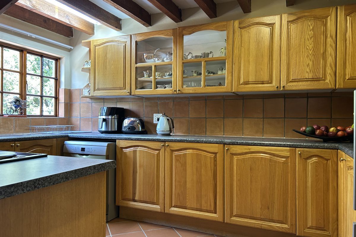 A traditional kitchen featuring warm wooden cabinetry, terracotta floor tiles, and exposed ceiling beams, offering a classic aesthetic with ample storage and counter space.
