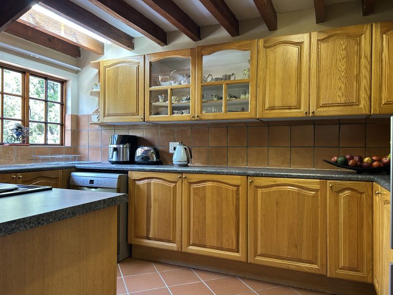A traditional kitchen featuring warm wooden cabinetry, terracotta floor tiles, and exposed ceiling beams, offering a classic aesthetic with ample storage and counter space.