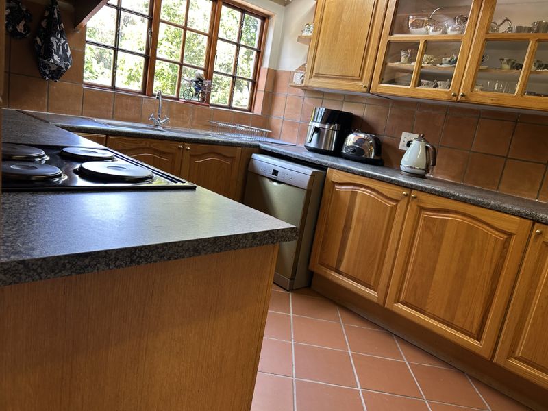 A functional kitchen featuring warm wooden cabinetry, granite-look laminate countertops, ceramic tile flooring, and a built-in electric hob with integrated dishwasher.