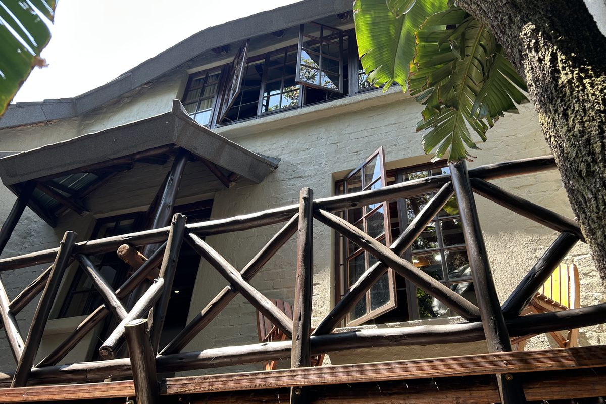 A rear exterior view of the property featuring a timber deck, rustic wooden balcony railing, and painted brick facade with casement windows.