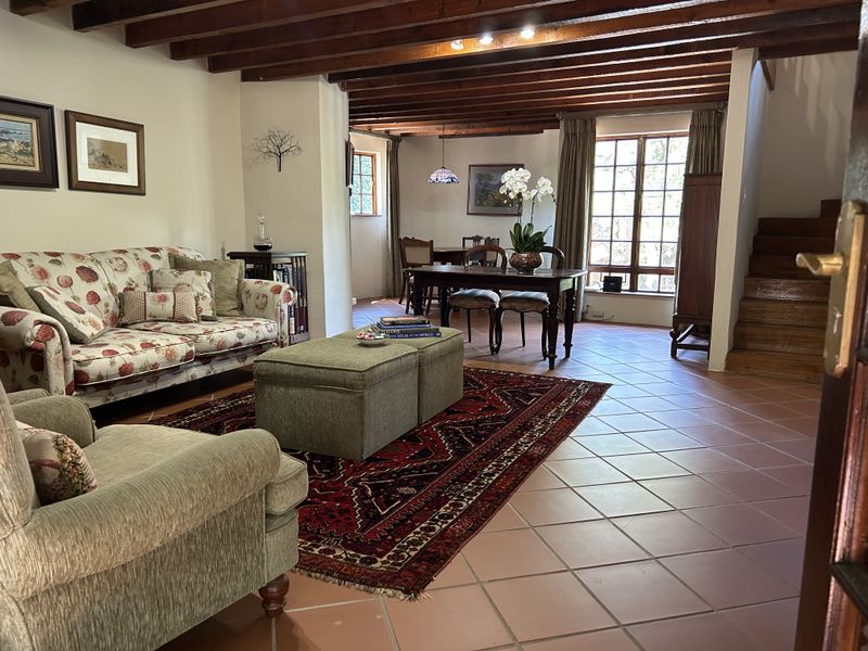 Spacious open-plan living and dining area featuring exposed timber ceiling beams, terracotta floor tiles, and a staircase leading to the upper level.