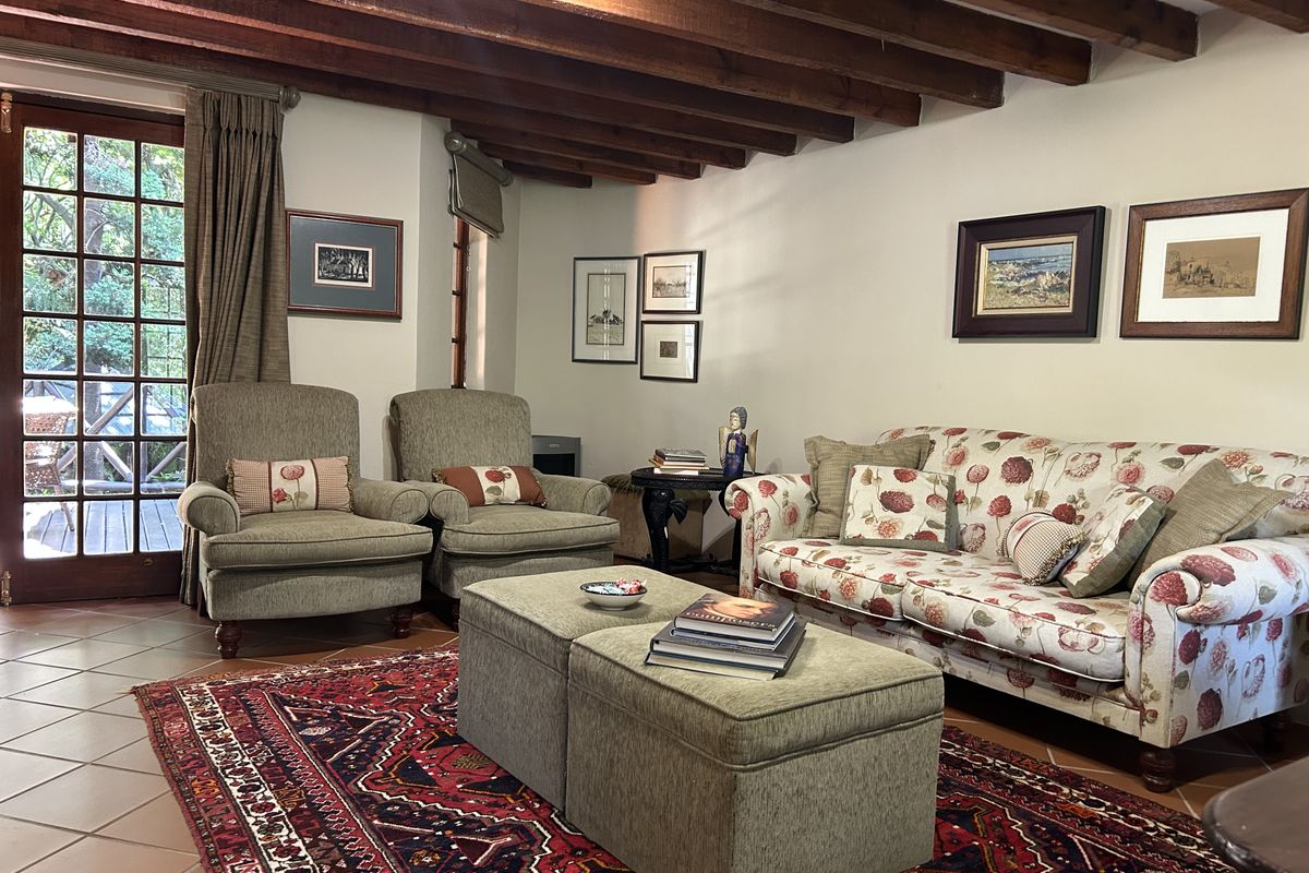 A cozy living room featuring exposed timber ceiling beams, terracotta floor tiles, and direct access to an outdoor patio through classic french doors.